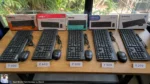 Five budget keyboard mouse combos arranged on wooden table with price tags in rupees, shot in natural Ahmedabad daylight